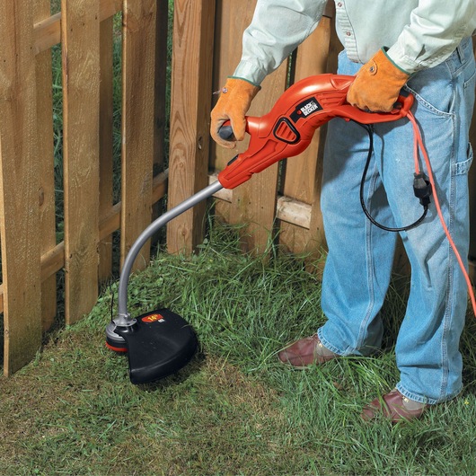 Photo of BLACKDECKER GH1100 electric string trimmer used on grass near a wooden fence.