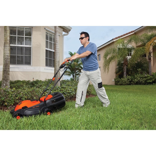 Photo of a person using a BLACKDECKER GR1000 lawn mower on green grass near a house, showing orange and black mower.