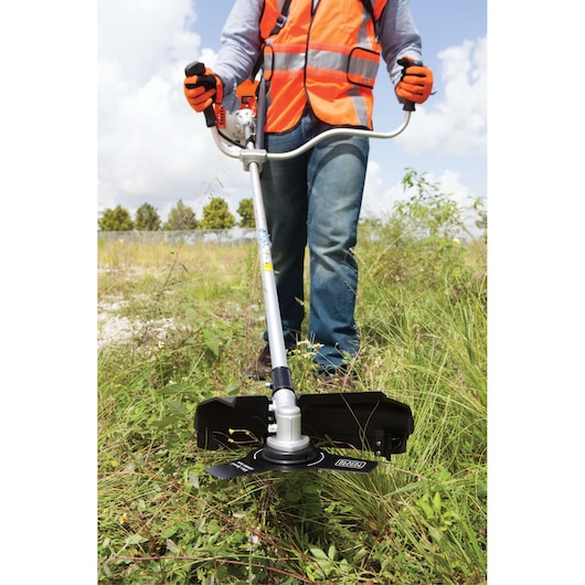Photo of BLACK+DECKER GST43 brush cutter in use outdoors, operator wearing orange safety vest and gloves.
