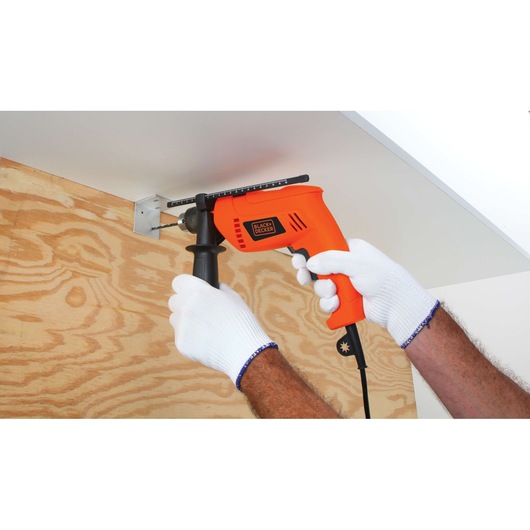 BLACKDECKER HD650 orange corded drill in use on wood panel, user wearing white gloves.
