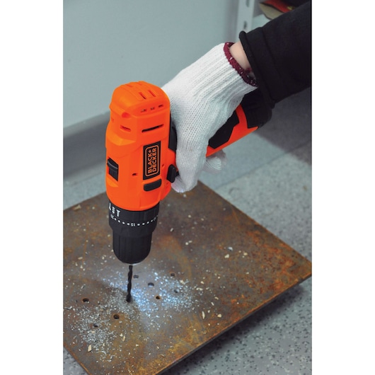 BLACK+DECKER HP12 cordless drill being used to drill metal plate, close-up view of tool in action.