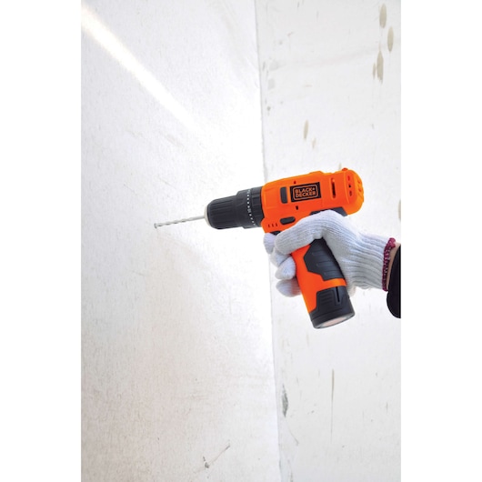 BLACKDECKER HP12 orange cordless drill in a gloved hand drilling into a white wall, side angle.
