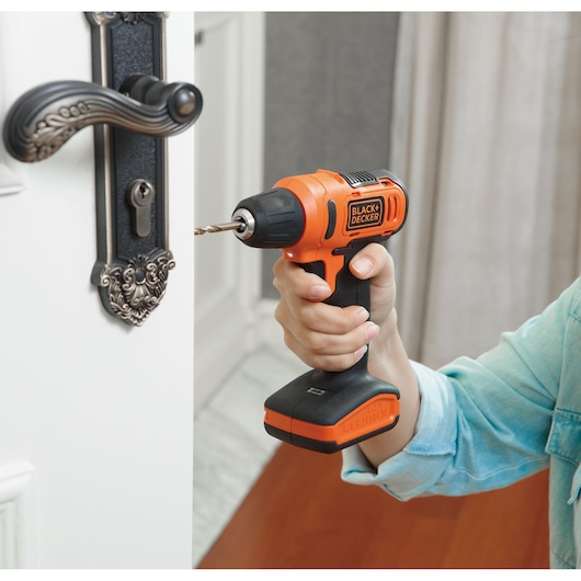 BLACK+DECKER LD12S cordless drill used to install metal door lock, person in blue shirt holding tool.
