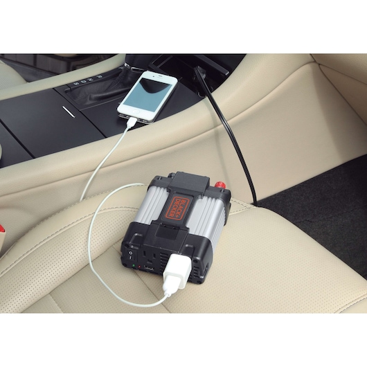 BLACKDECKER PI400LA power inverter charging a smartphone in a car interior on beige leather seat.