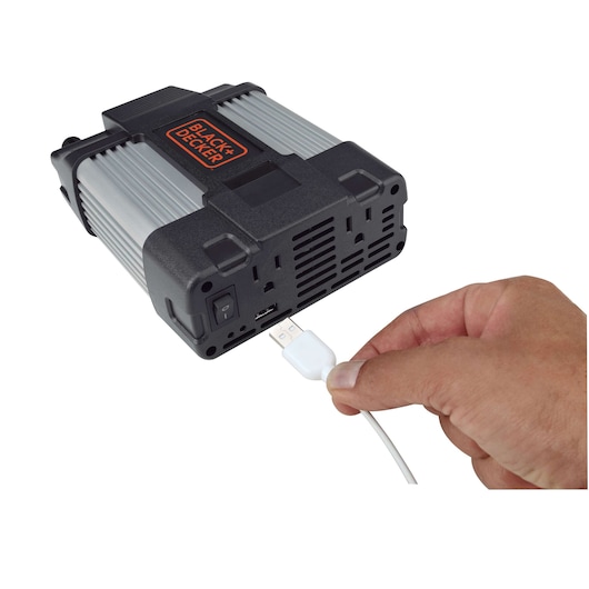 Photo of BLACK+DECKER PI750LA power inverter with a hand plugging a USB cable into the front USB port, white background.
