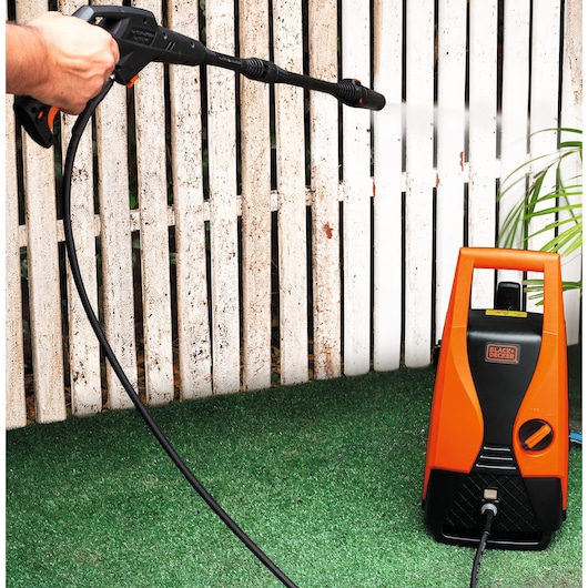 BLACKDECKER PW1450TD pressure washer in use cleaning white fence, orange and black unit on green grass.