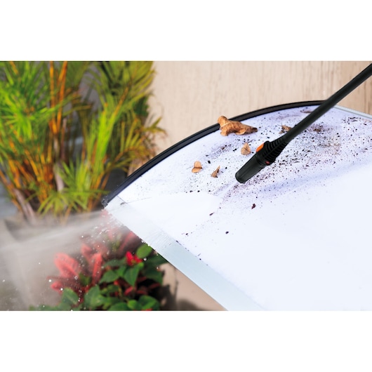 BLACKDECKER PW1450TD pressure washer cleaning dirty surface with water spray, plants in background.